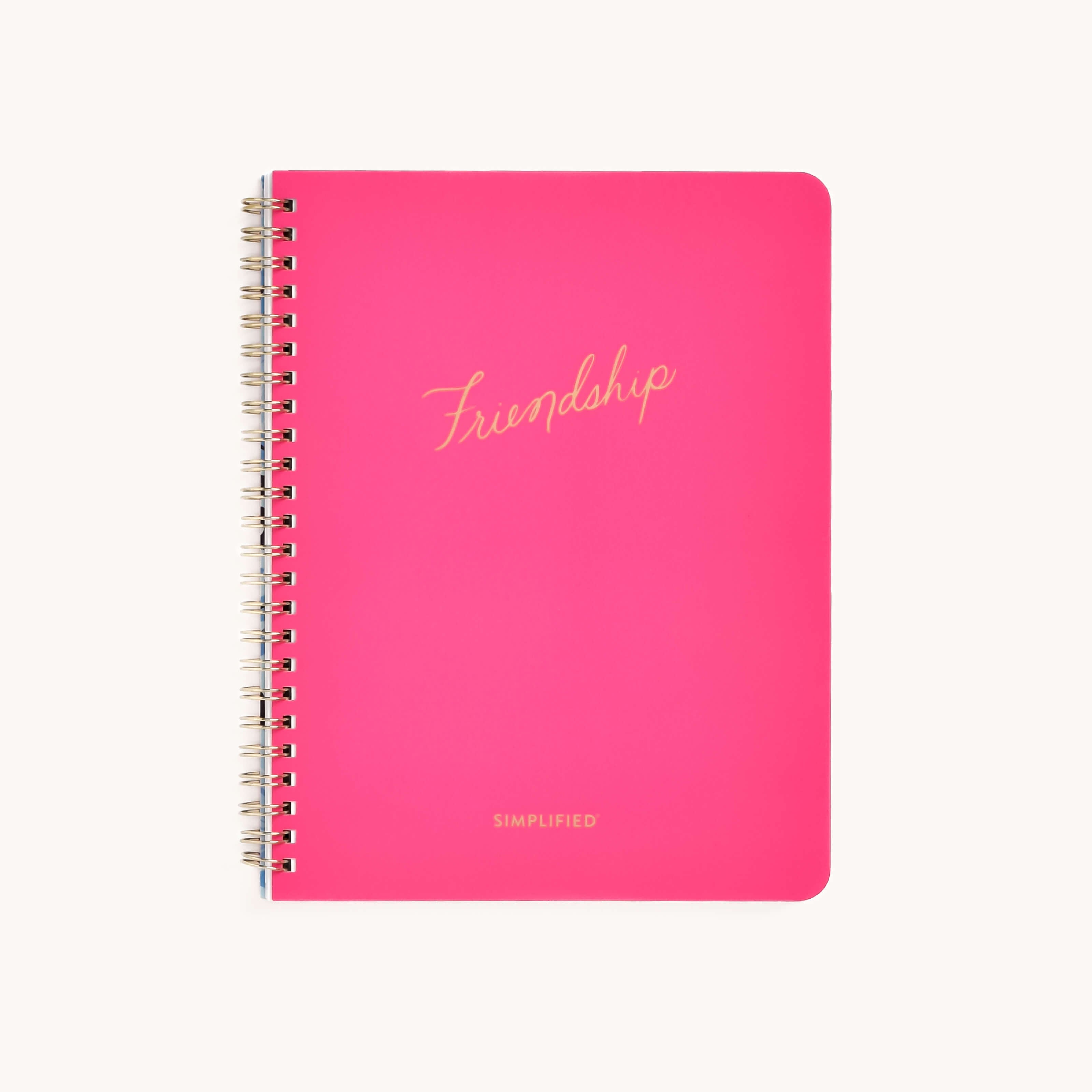 A vibrant pink spiral-bound notebook titled Friendship features SIMPLIFIED in gold cursive on the cover, underlining actionable plans. Its clean white backdrop emphasizes both lasting connection and personal growth.
