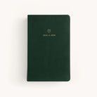 The Simplified 2025-2026 Bookbound Daily Dapperdesk Planner in Evergreen features a green leather-bound cover with rounded corners. It includes a small gold emblem and 2025 to 2026 text in gold, centered on the front, making it perfect for detailed planning against a light background.