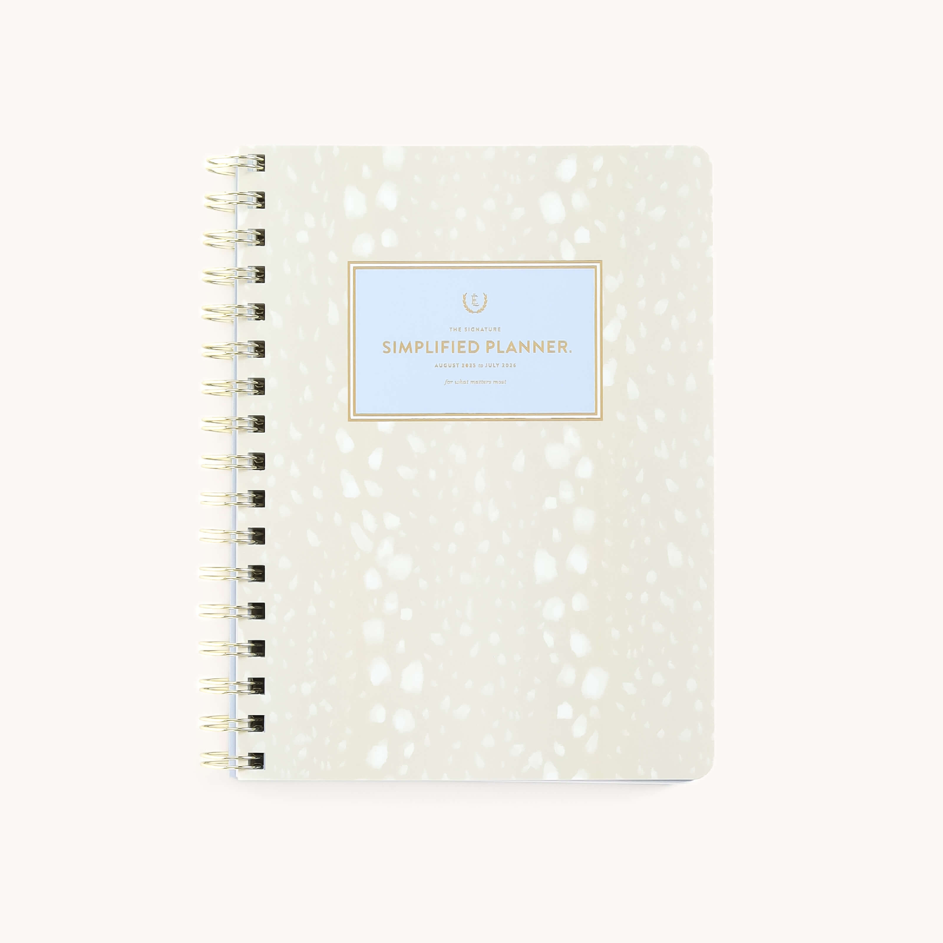 A stylish spiral-bound planner with a white and ivory abstract cover, labeled 2025-2026 Softcover Weekly Simplified Planner - Ivory Antelope by Simplified, features a light blue square adorned with shimmering gold foil.