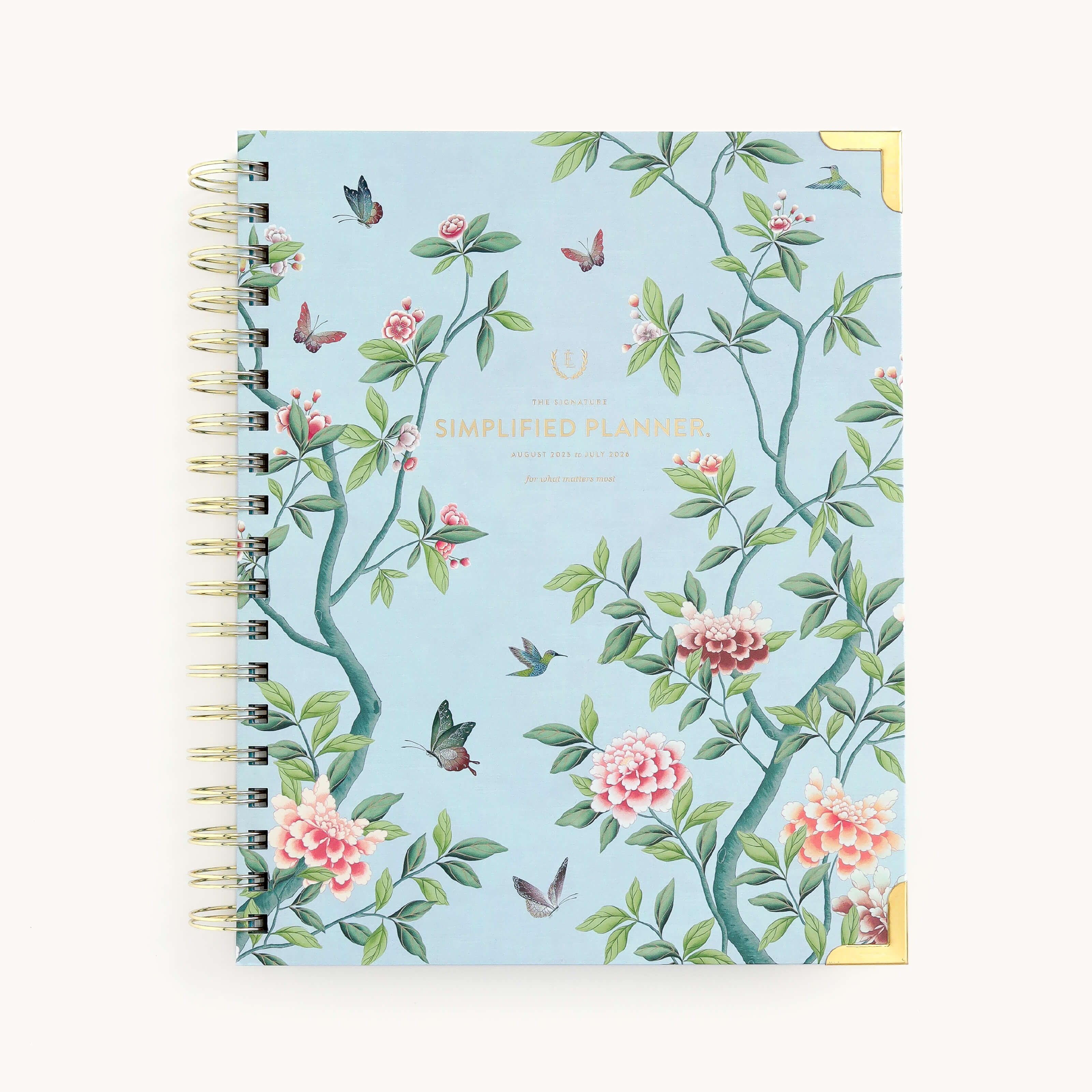 The 2025-2026 Spiral Weekly Simplified Planner - Faraway Land by Simplified features a light blue cover with colorful floral and bird designs, accented with gold foil. The title Simplified Planner is printed in gold at the center, and chic gold accents reinforce the corners.