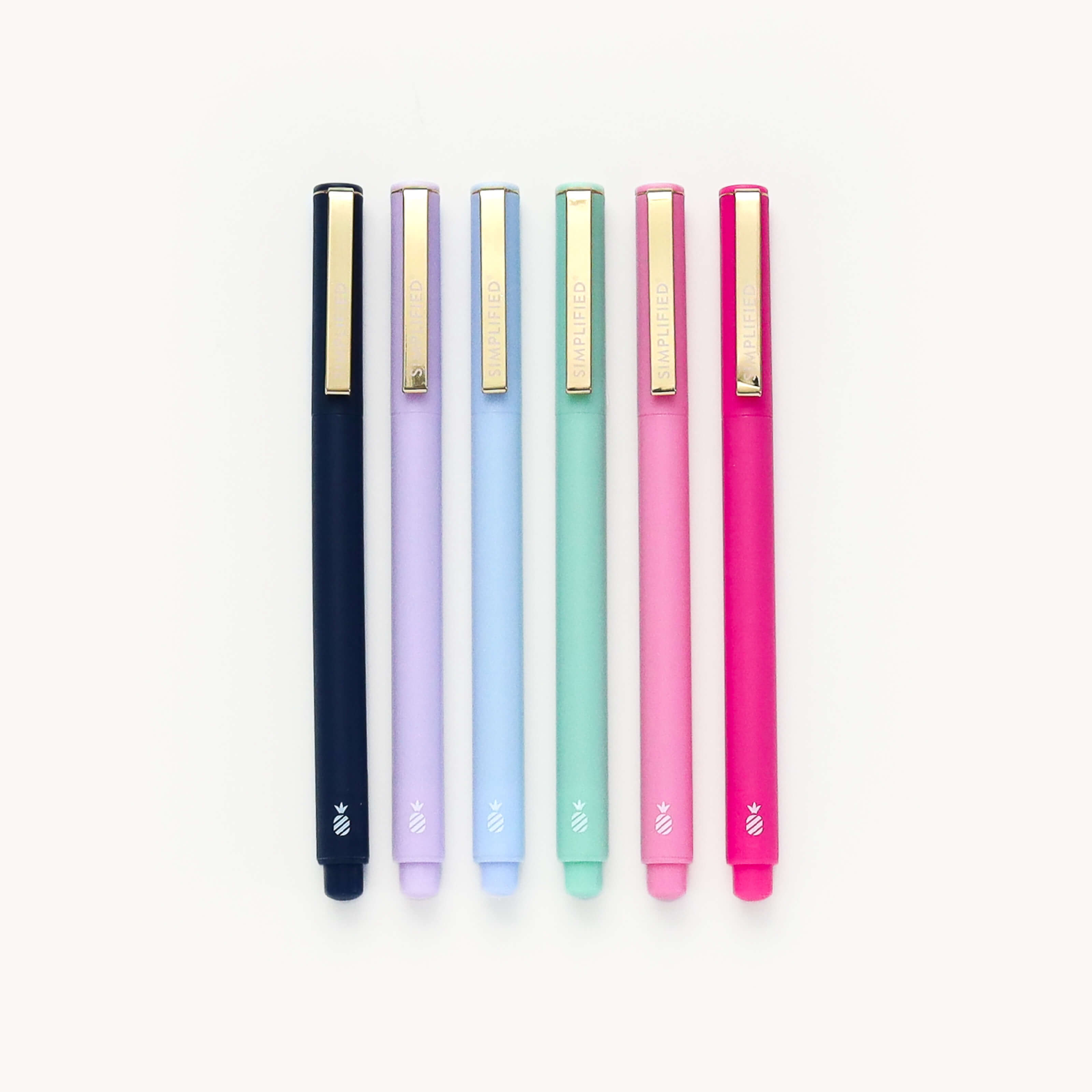 Simplified Felt-Tipped Pen Set by Emily Ley, featuring six pens in navy, lilac, light blue, sage green, blush pink, and raspberry, each with a gold metal clip and white pineapple logo.