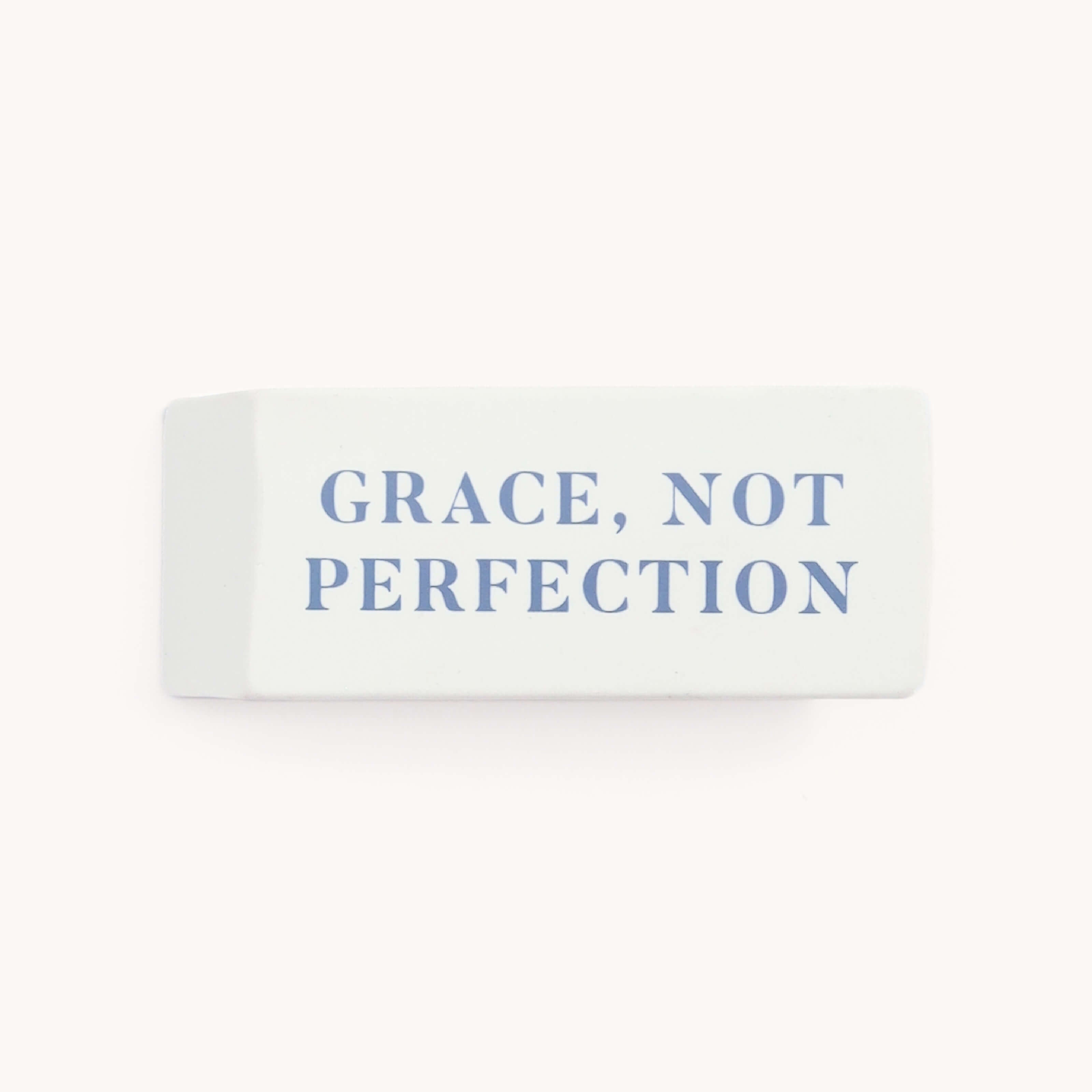 The Simplified Jumbo Eraser, a white rectangle with the blue text GRACE, NOT PERFECTION on top, is the perfect desktop accessory against a plain, light background.