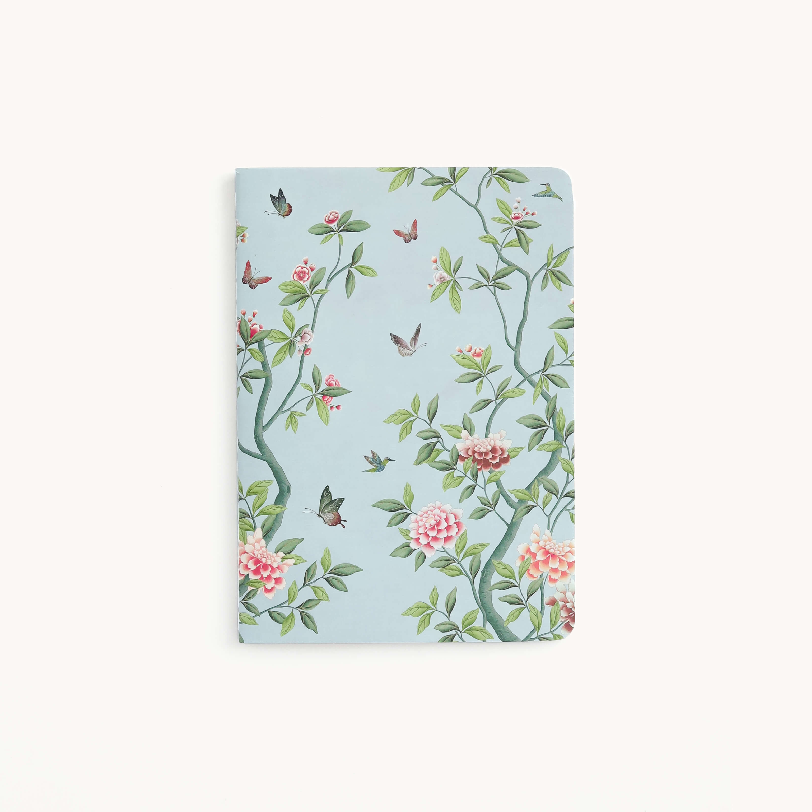 The Mini Notebook - Faraway Land by Simplified features a light blue cover with custom floral and bird designs, combining green branches, pink flowers, and colorful hummingbirds on a white background for a charming and serene nature-themed pattern.