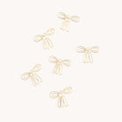 The image displays six gold Paper Clips - Bows by Simplified, resembling simple ribbon designs with two loops and tails, scattered on a white background.