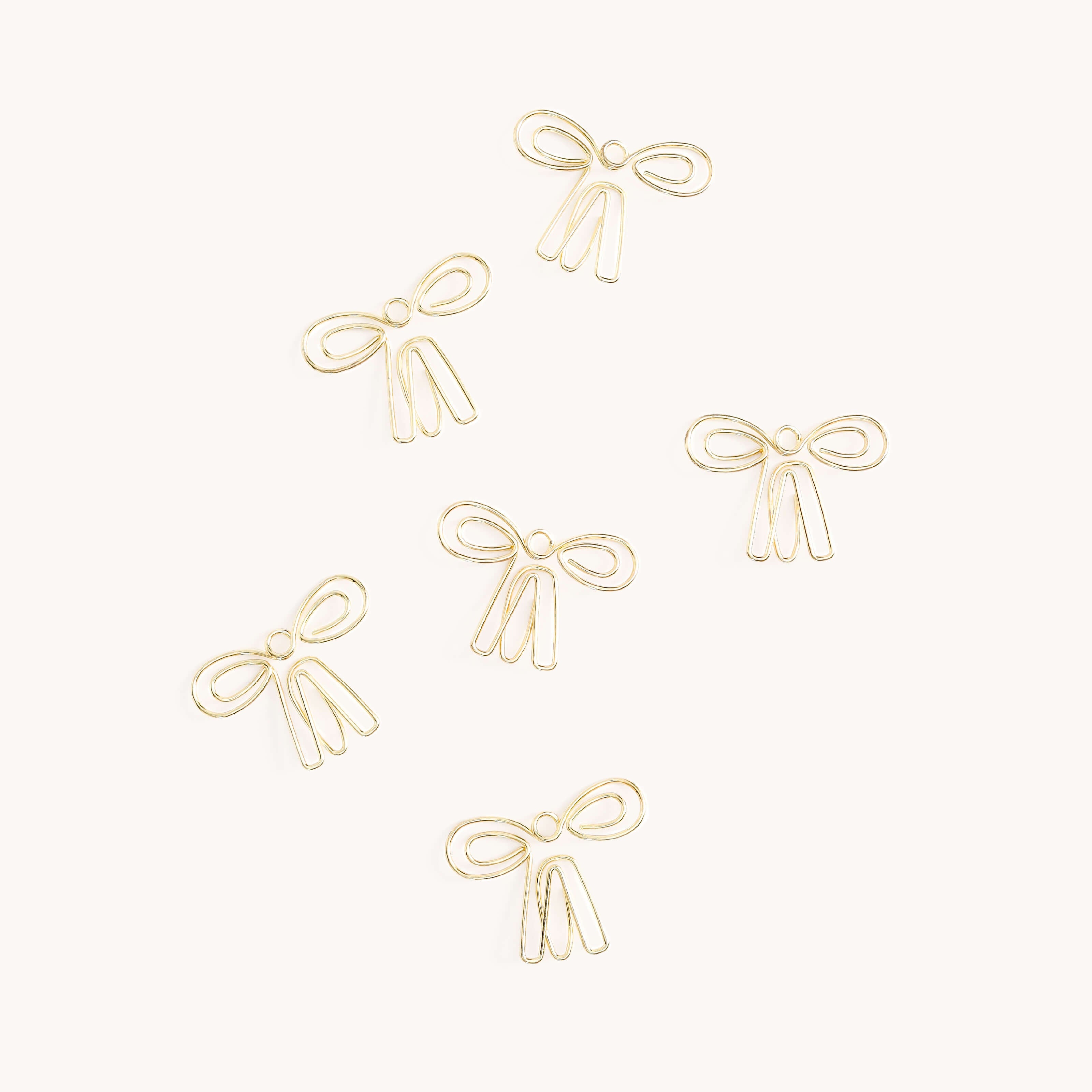 The image displays six gold Paper Clips - Bows by Simplified, resembling simple ribbon designs with two loops and tails, scattered on a white background.