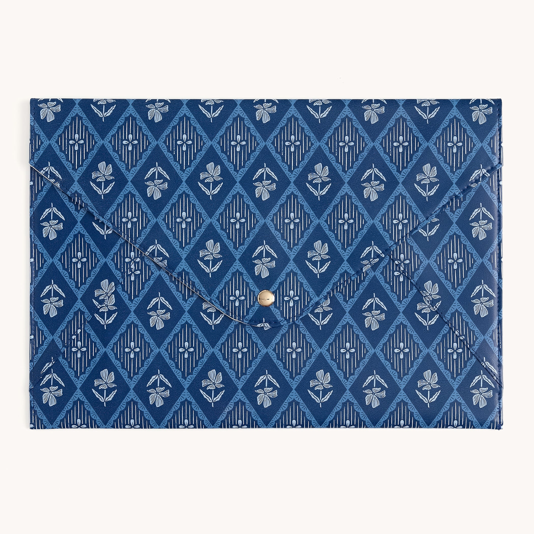 The Simplified Leatherette Tech Case - Block Floral is a blue envelope-style case with a diamond pattern, white floral motifs, and a central gold button closure.