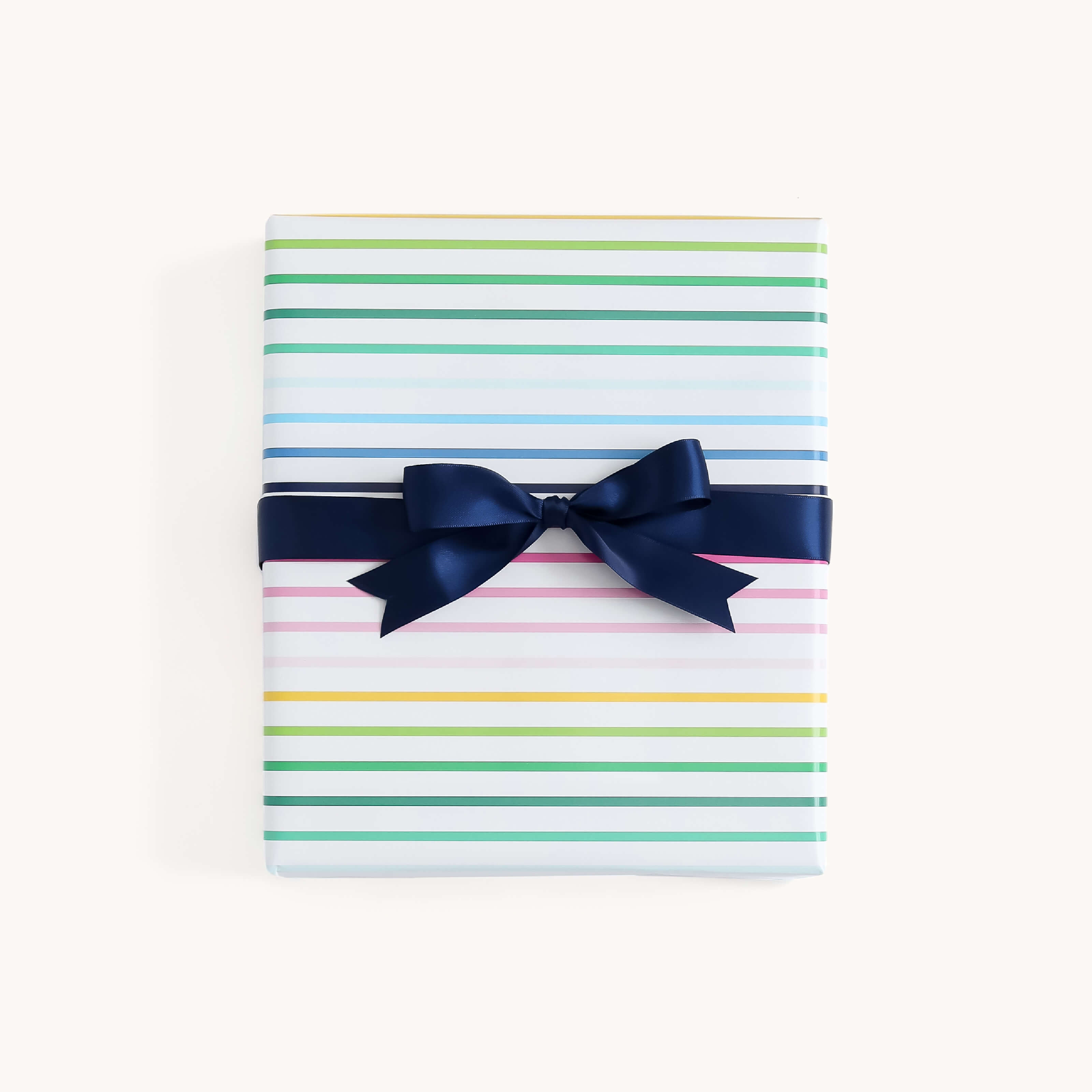 The Simplified Gift Wrap Roll - Happy Stripe features white paper with colorful horizontal stripes and gold foil accents, finished with a dark blue ribbon—an ideal choice for holiday gifts.