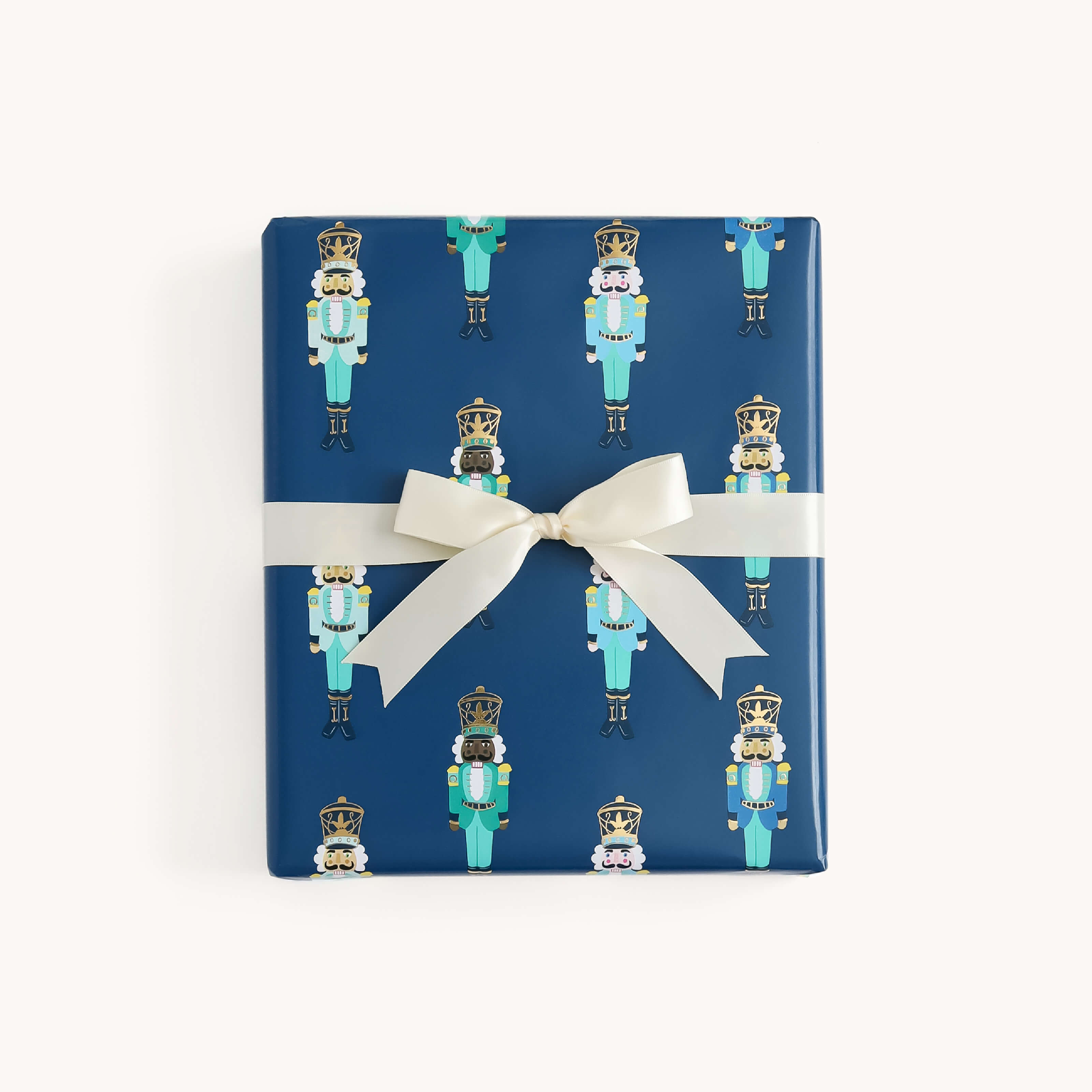 A square gift box wrapped in the Simplified Gift Wrap Roll - Nutcrackers, featuring repeating nutcracker soldier designs and finished with a white ribbon—ideal for festive holiday gifts.