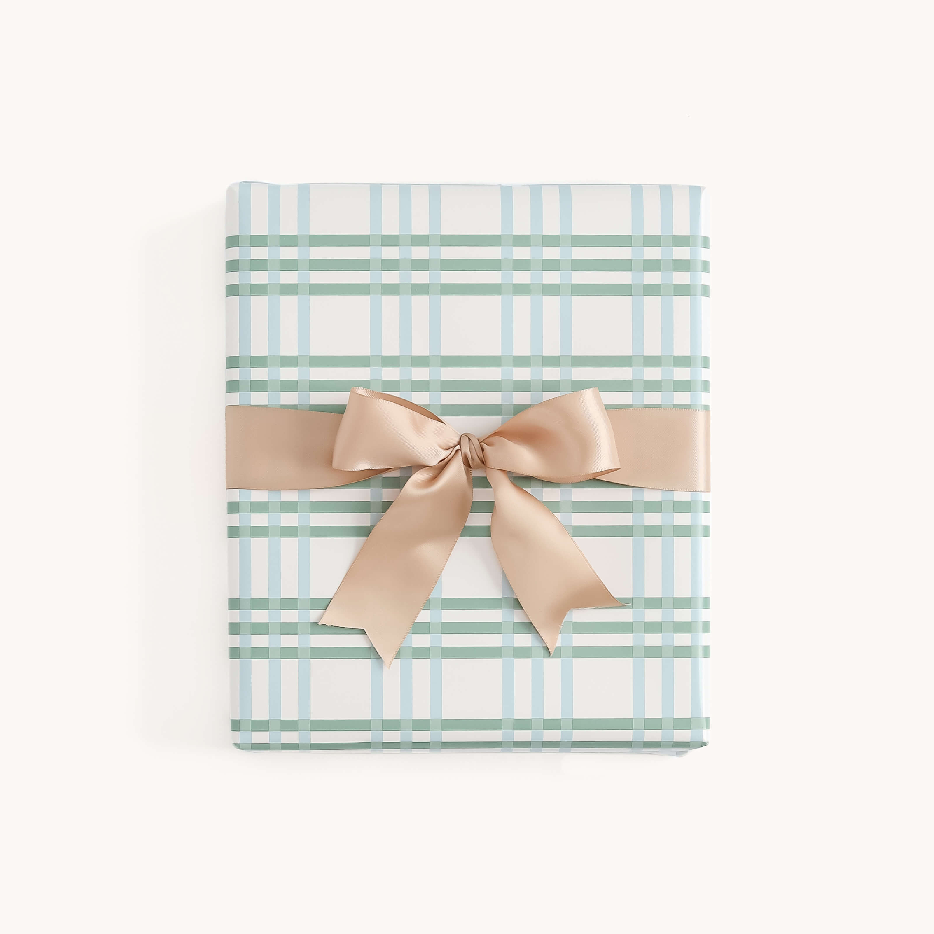 A rectangular holiday gift wrapped in Simplified’s Gift Wrap Roll - Pistachio Plaid, featuring blue and green plaid on white, finished with a wide shiny beige satin ribbon and bow, against a plain light background.