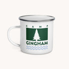 The Simplified Enamel Mug - Camp Gingham features a white enamel body with a metal rim, green rectangle and pine tree design, CAMP GINGHAM text, blue wavy lines—lightweight and perfect for summer camp adventures.