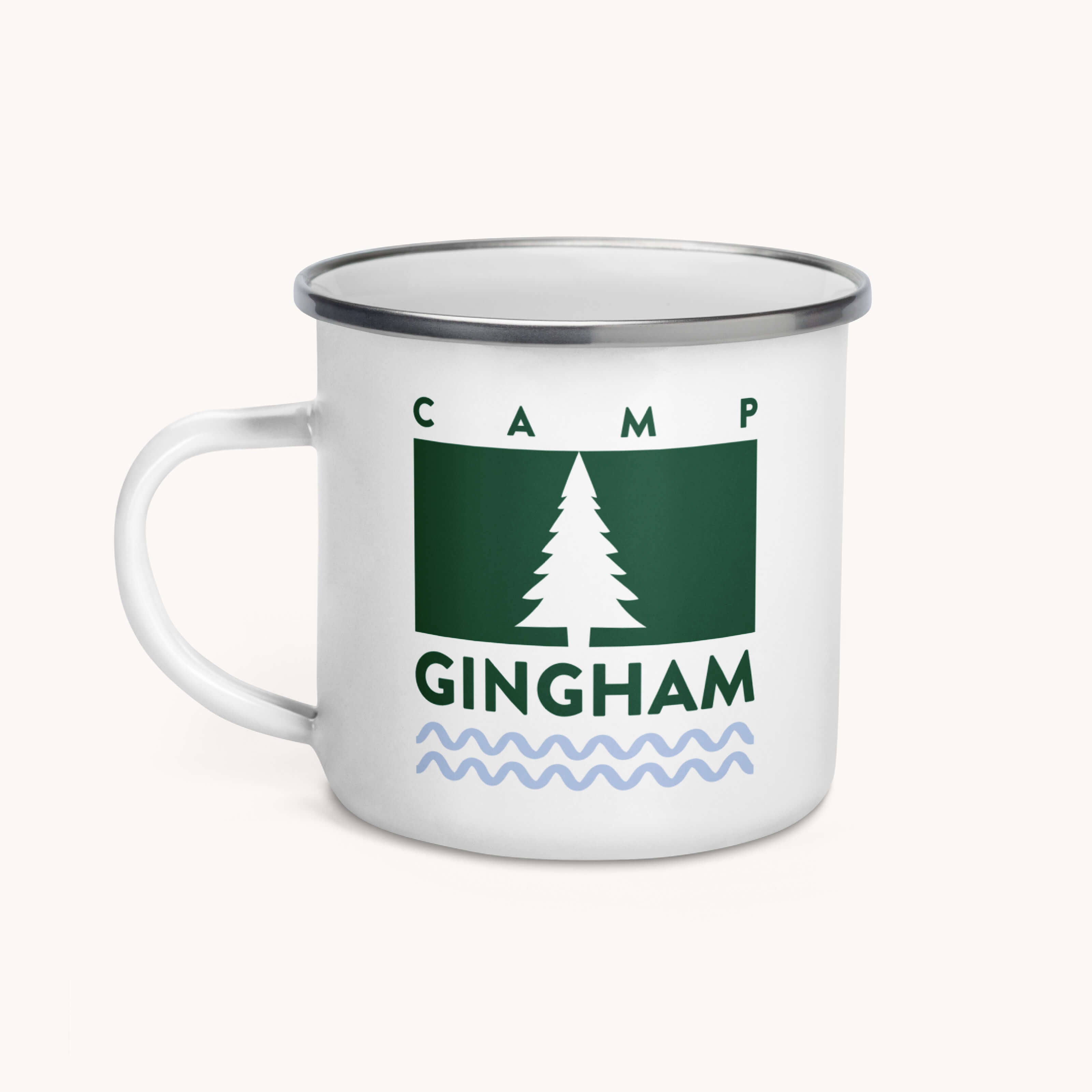 The Simplified Enamel Mug - Camp Gingham features a white enamel body with a metal rim, green rectangle and pine tree design, CAMP GINGHAM text, blue wavy lines—lightweight and perfect for summer camp adventures.