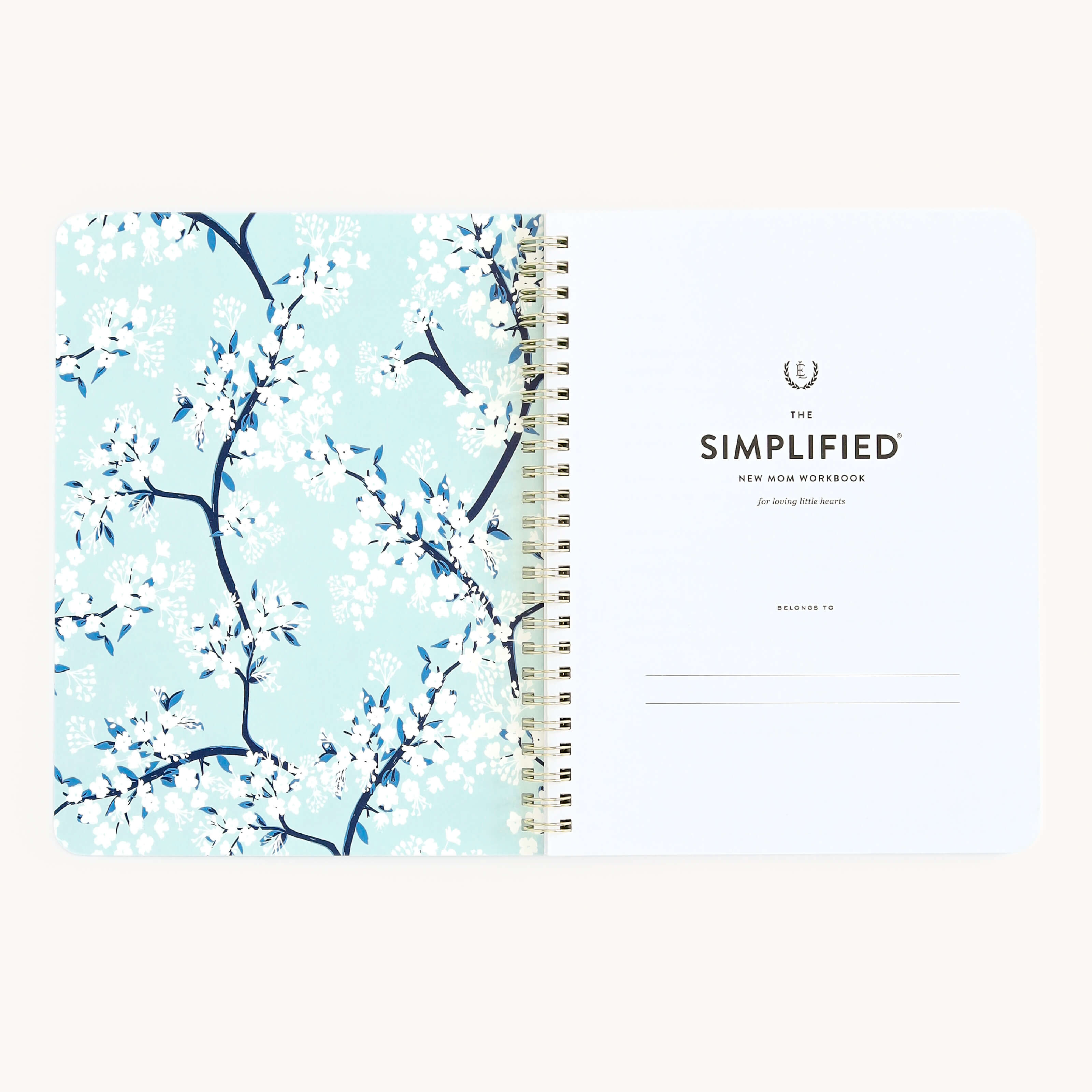 The Workbook - New Motherhood by Simplified features a right page with a blank Belongs to line, while the left page has a light blue background adorned with blue and white flowers—ideal for busy parents to organize their thoughts.