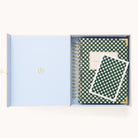 An open blue gift box reveals a Simplified 2026 Spiral Daily Simplified Planner in Camp Gingham (green and white checked with gold accents) and a matching card, both neatly arranged inside.
