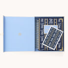 A blue gift box cradles a Simplified 2025-2026 Spiral Daily Planner featuring a navy cover with white bows and lines, paired with a matching card. The light blue lid is adorned with gold foil details.