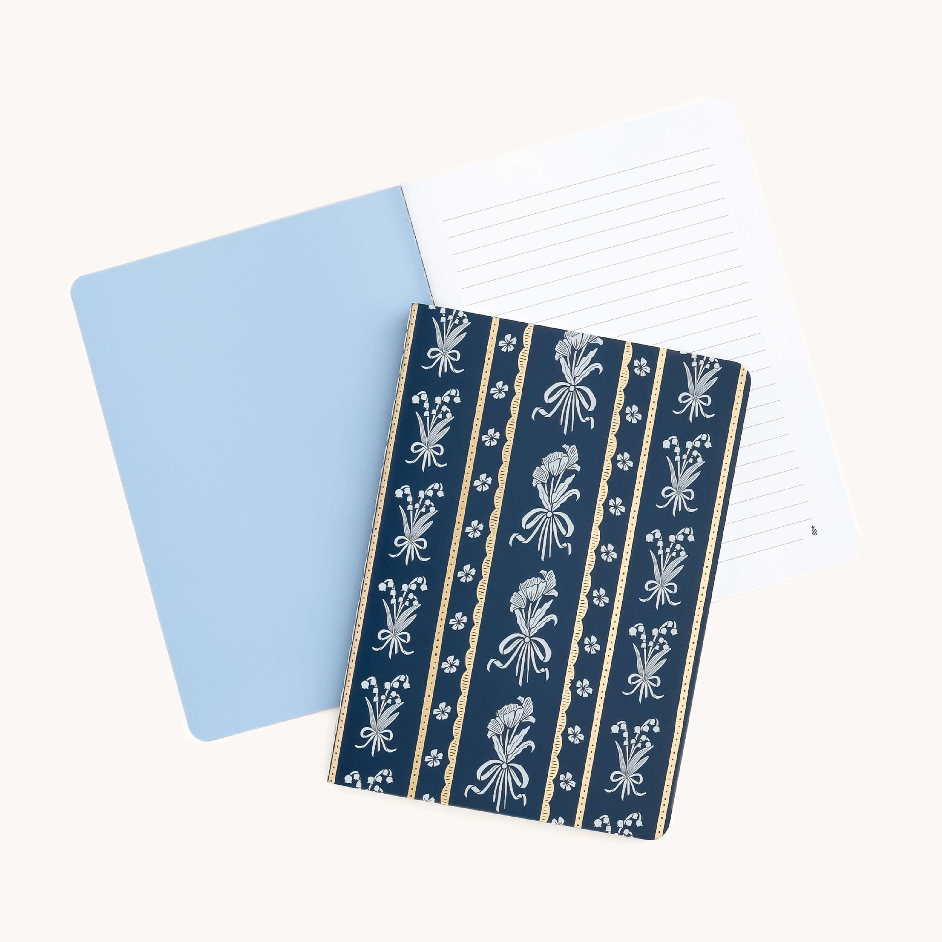 The Mini Notebook - Poppy Posies by Simplified showcases a blue interior with lined pages. Its partially closed cover features vertical stripes adorned with intricate white floral patterns on a dark blue background, resting atop the lined section.