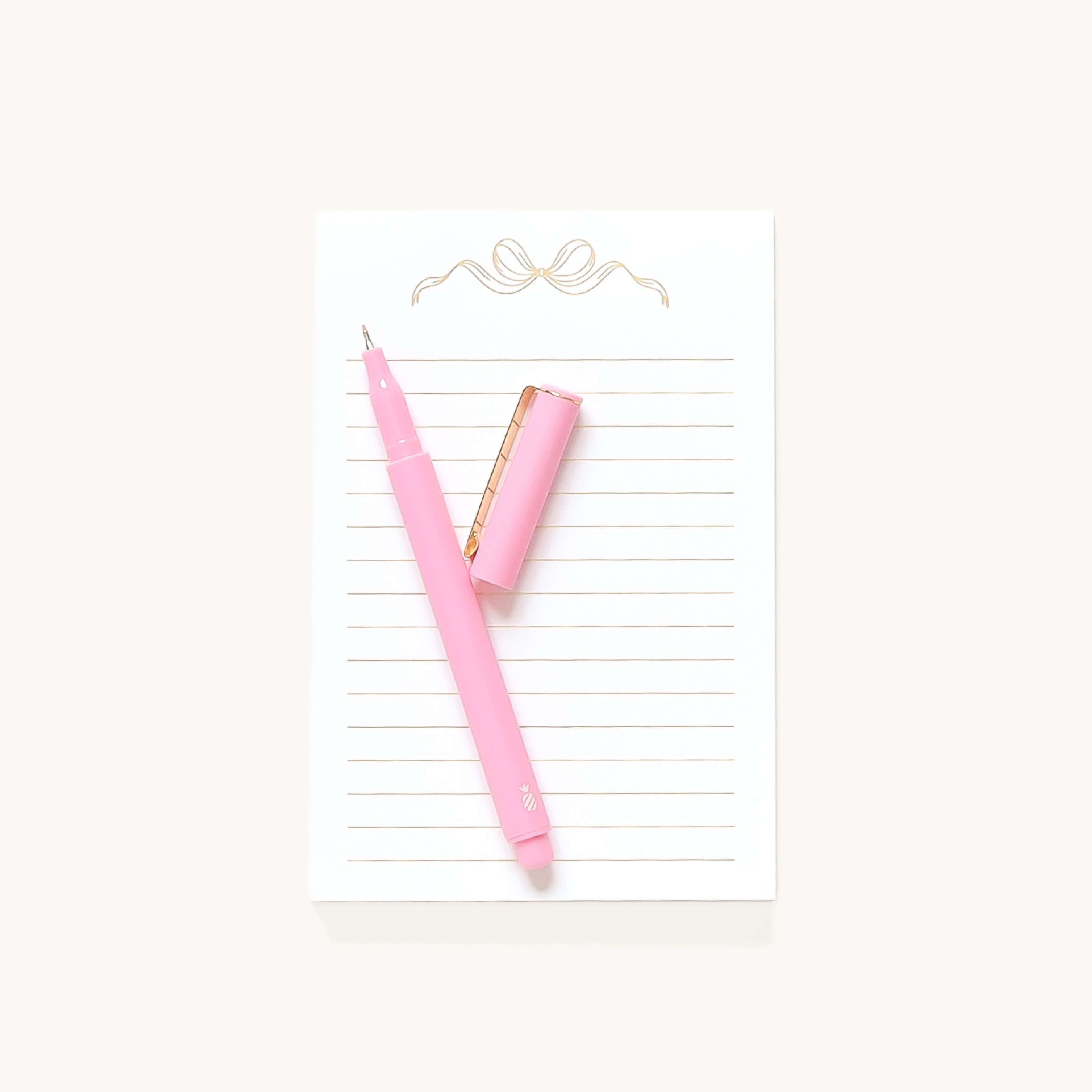 The Simplified Lined Notepad - Gold Bow features elegant gold lines, a decorative gold bow at the top, and comes with a pink pen—a chic desk accessory or thoughtful gift.
