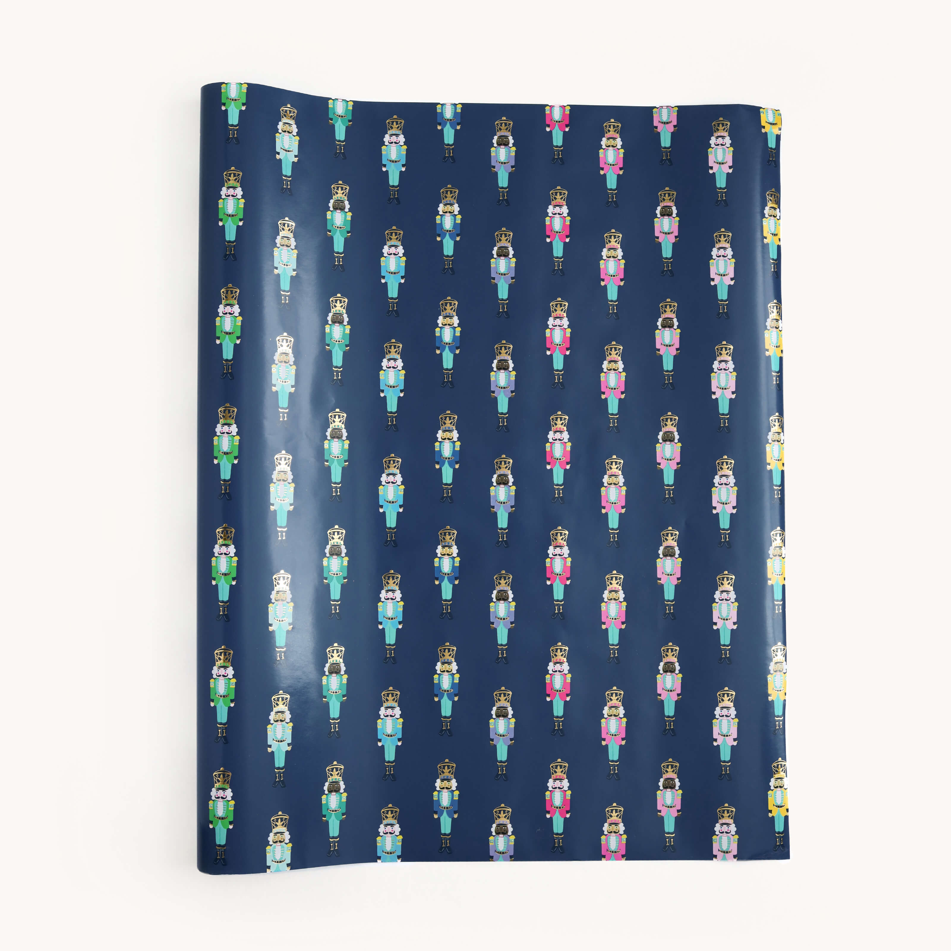 The Simplified Gift Wrap Roll - Nutcrackers features a repeating pattern of colorful nutcrackers on a dark blue background. Perfect for holiday gifts, the roll may arrive slightly curled at the edge.