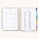 The 2026 Spiral Daily Simplified Planner by Simplified in Camp Gingham features gold spiral binding, colorful index tabs, the 2026 yearly calendar on the left, and a list of 2026 holidays on the right—ideal for organizing your year.