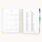 The 2026 Spiral Daily Simplified Planner - Serene Stripe by Simplified features gold metal corners, spiral binding, and colorful tab dividers. Inside, see a 2026 yearly calendar on the left and a holiday list on the right—ideal for planner fans.