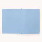 A 2025-2026 Bookbound Weekly Dapperdesk Planner by Simplified, featuring a light blue leatherette cover with blank pages, lies flat on a white surface.