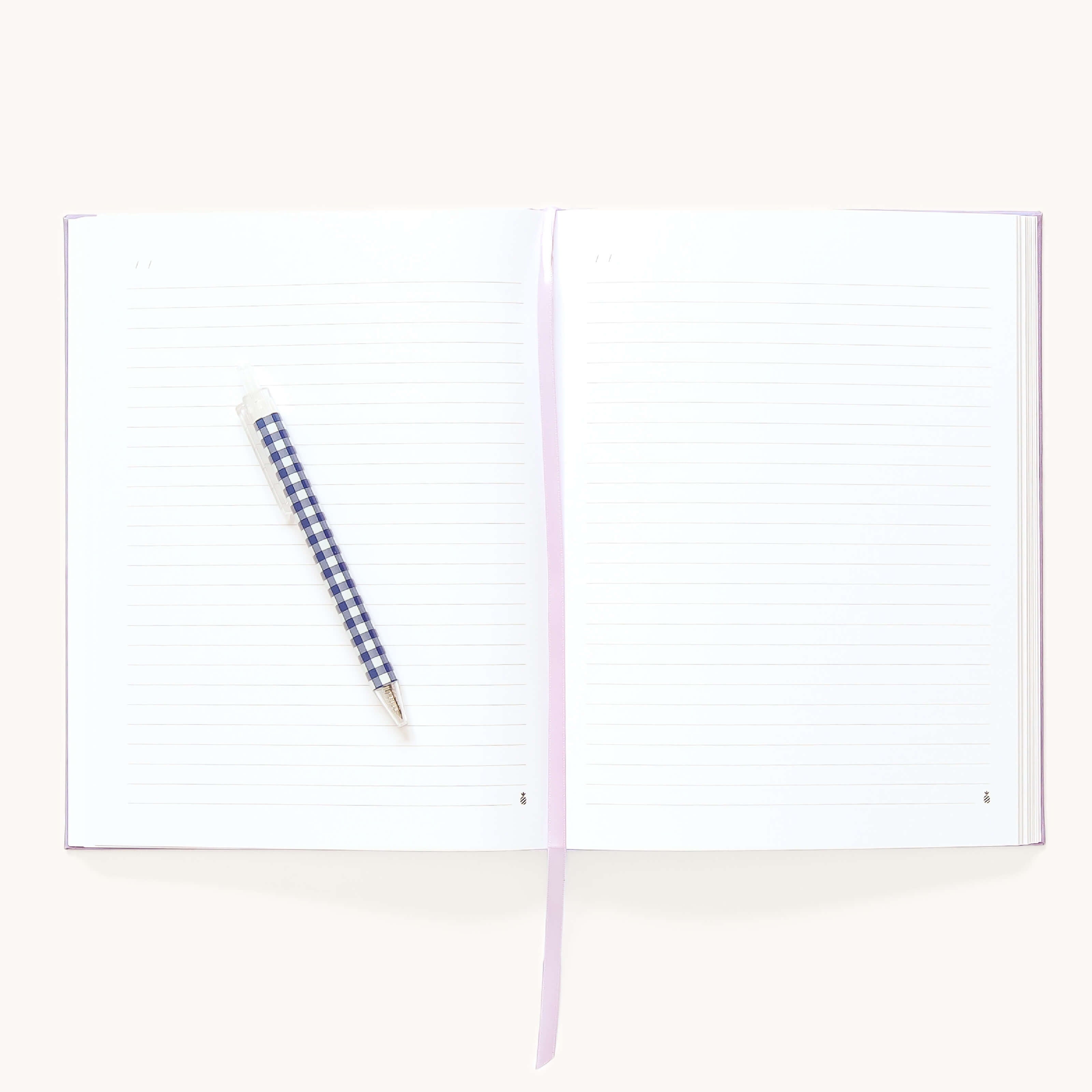 The Simplified Linen Journal - Celestial features open lined pages, a blue and white checkered pen on the left page, and a light purple ribbon bookmark across the center.
