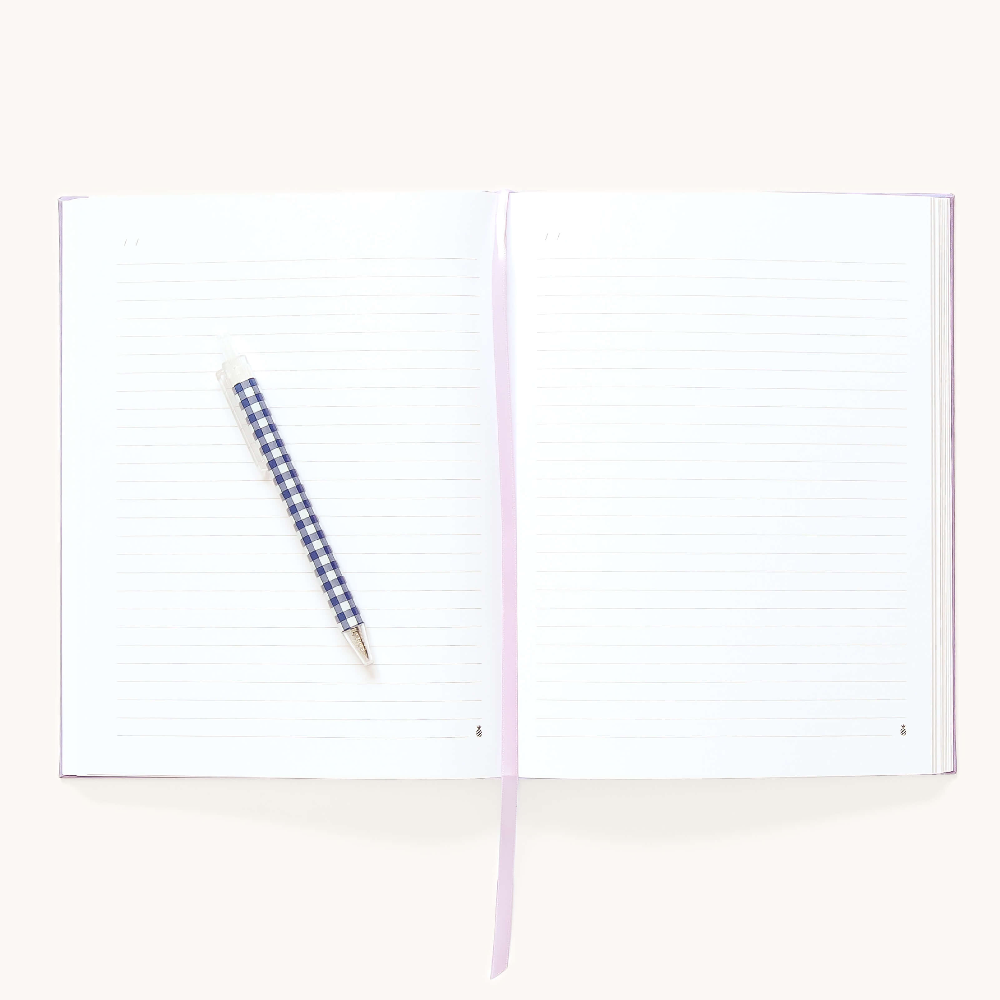 The Simplified Linen Journal - Celestial features open lined pages, a blue and white checkered pen on the left page, and a light purple ribbon bookmark across the center.