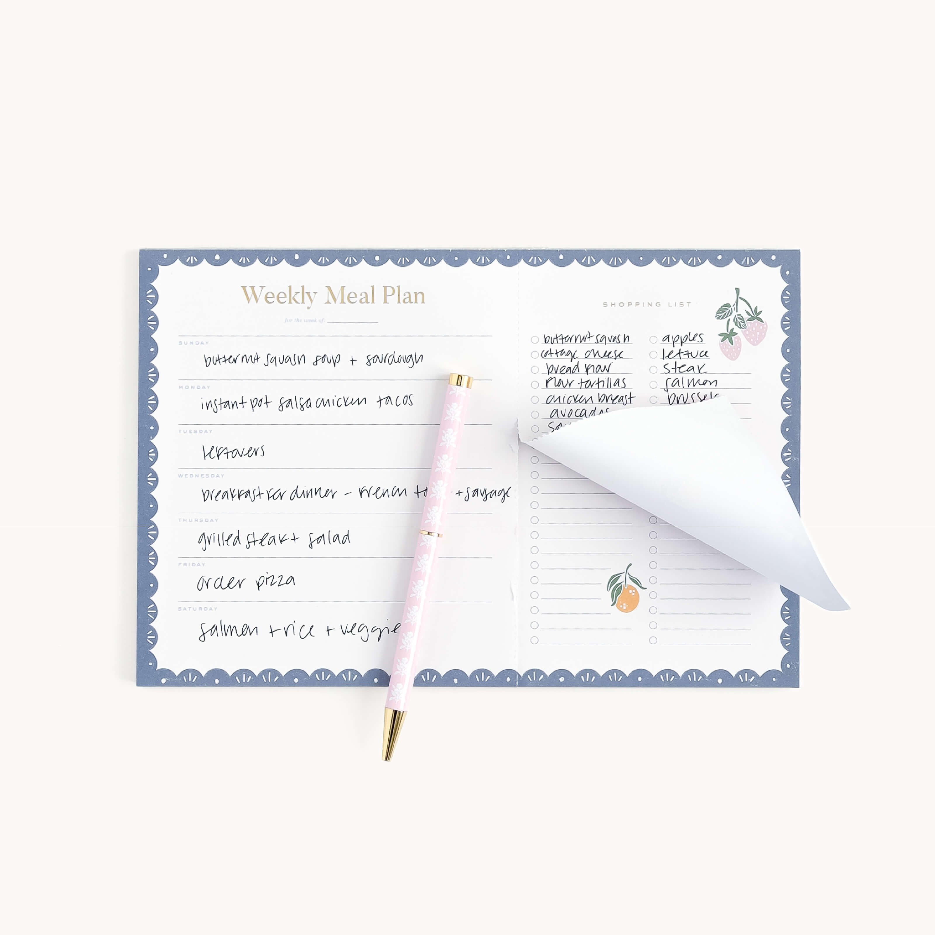 The Simplified Meal Planning Notepad is open with a handwritten weekly meal plan and a blue-bordered grocery list in white text. A pink pen with gold accents rests on partially flipped pages.