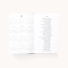 The 2025-2026 Bookbound Daily Dapperdesk Planner - Carolina Dot by Simplified features a sleek leatherette cover. The left page presents a gridded year overview with months and dates, while the right lists holidays in two columns. Its minimalist design complements the plain background elegantly.