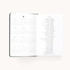 The 2025-2026 Bookbound Daily Dapperdesk Planner - Evergreen by Simplified features a yearly calendar grid on the left page and detailed descriptions of holidays and notable dates on the right. Its pristine white background enhances its clean design, ideal for daily planning enthusiasts.