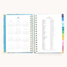 The open spiral-bound 2025-2026 Daily Simplified Planner by Simplified features a calendar on the left and holiday list on the right. It boasts gold foil accents, colorful tabs for sections like Prep Work pages, and a vibrant blue cover with gold corners.