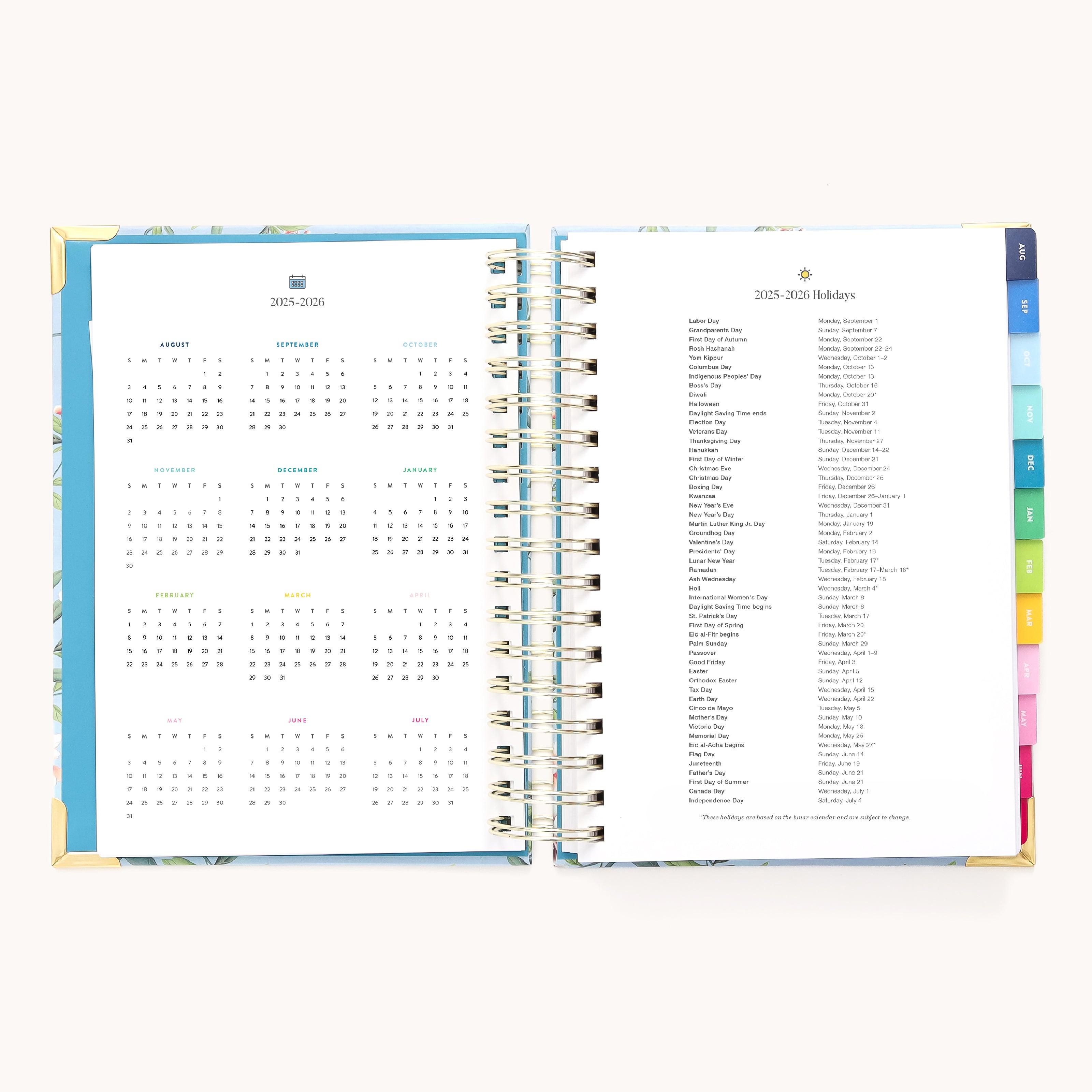 The open spiral-bound 2025-2026 Daily Simplified Planner by Simplified features a calendar on the left and holiday list on the right. It boasts gold foil accents, colorful tabs for sections like Prep Work pages, and a vibrant blue cover with gold corners.