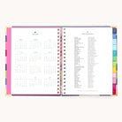 The 2025-2026 Spiral Weekly Simplified Planner - Rainbow Row by Simplified displays a yearly calendar on the left and a holiday list on the right. It boasts colorful tabbed edges and elegant gold foil details, providing beautifully organized pages to guide your year.