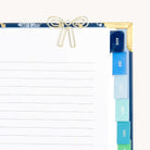 A decorative clipboard by Simplified features a durable metal bow-shaped paper clip holding lined paper. Colorful monthly tabs from August to January line the right edge. It boasts a floral design with gold corners. The product used for securing papers is called Paper Clips - Bows.
