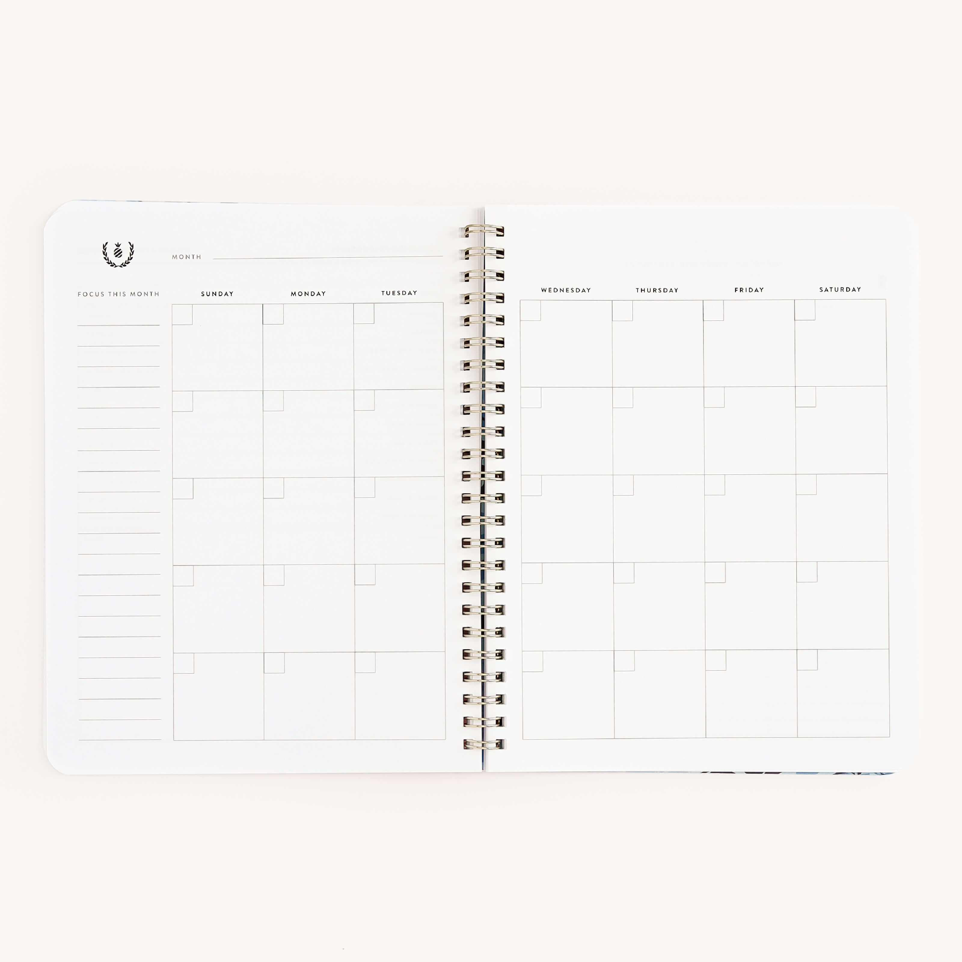 The Simplified Workbook - Friendship is an open spiral-bound planner with a blank monthly calendar spread. The left page includes a Focus This Month section for notes, with weekdays labeled and empty squares for plans and goals.