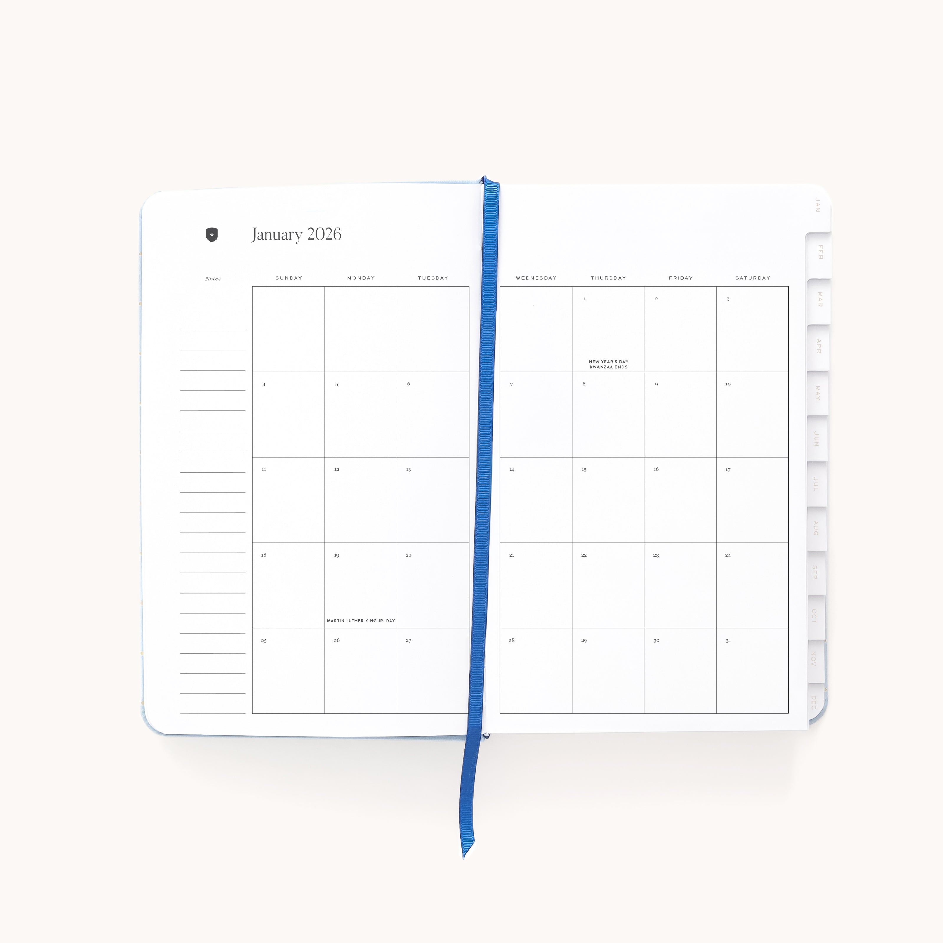 The Simplified 2026 Bookbound Daily Dapperdesk Planner in Carolina Dot is open to January 2026, showing a minimalist layout with mostly blank pages, a blue ribbon bookmark down the center, and tabbed dividers on the right.