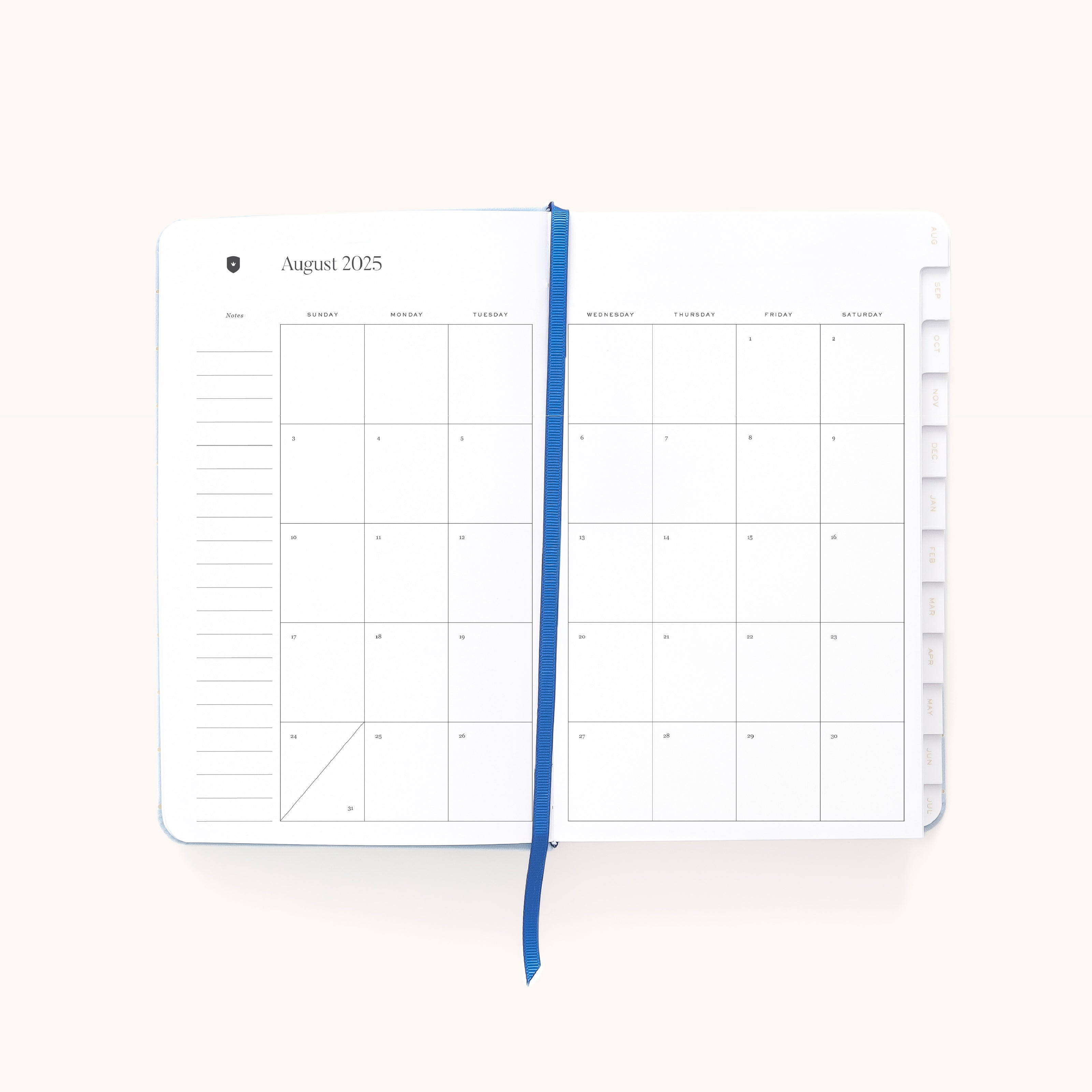 The Simplified 2025-2026 Bookbound Daily Dapperdesk Planner in Carolina Dot, featuring a leatherette cover, showcases an August 2025 monthly calendar. It includes a blue ribbon bookmark with dates from Sunday to Saturday and ample note space on the left, against a plain white background.