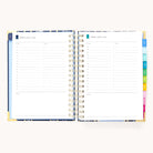 The 2025-2026 Spiral Daily Simplified Planner - Poppy Posies by Simplified, adorned with gold foil details, shows pages for Monday, August 7, and Tuesday, August 8. Each page has hourly slots from 6 AM to 8 PM and a notes section. Colorful tabs adorn the right edge of this planner.