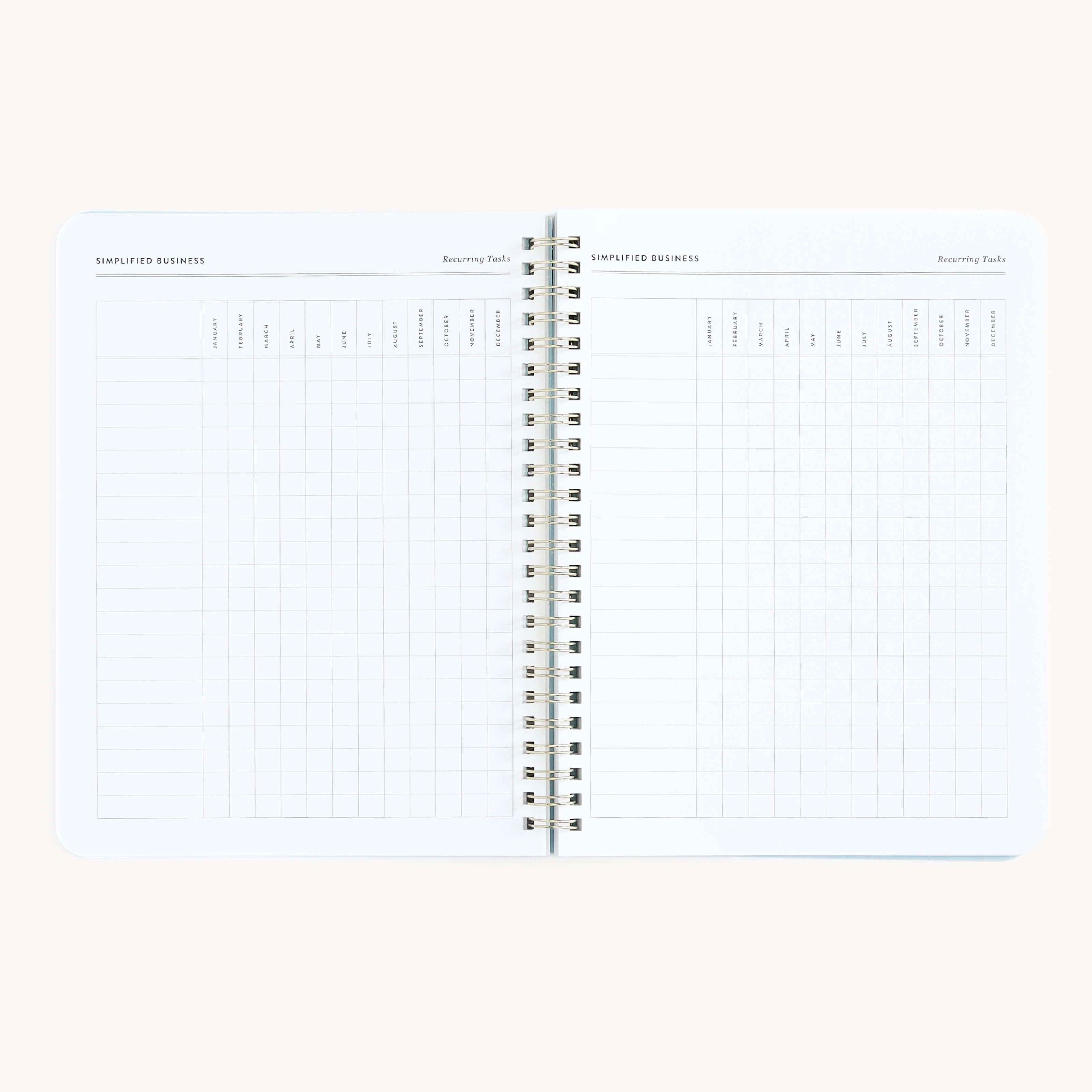 The Workbook - Entrepreneurship by Simplified is a spiral-bound planner with grid pages featuring monthly columns, ideal for planning routines and tracking tasks. Its organized layout provides ample space for notes and rests on a plain light background.