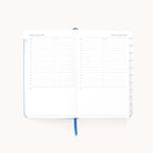 The Simplified 2025-2026 Bookbound Daily Dapperdesk Planner - Carolina Dot features pages for Sunday, August 3, and Monday, August 4, 2025. Each day has hourly slots from 7 AM to 8 PM with note sections. A blue ribbon marks your spot in this leatherette planner designed for organization and ease with side tabs.