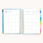 The 2025-2026 Spiral Daily Simplified Planner - Faraway Land by Simplified has an open spread with a monthly calendar for August 2025 on the left and notes on the right. Its colorful tab dividers and gold foil details add elegance, perfect for task and plan management.