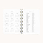 An open 2025-2026 Softcover Weekly Simplified Planner by Simplified in Happy Stripe design features organized pages with a full calendar for 2025-2026 on the left and a list of holidays for 2025-2026 on the right, set against a plain white background.