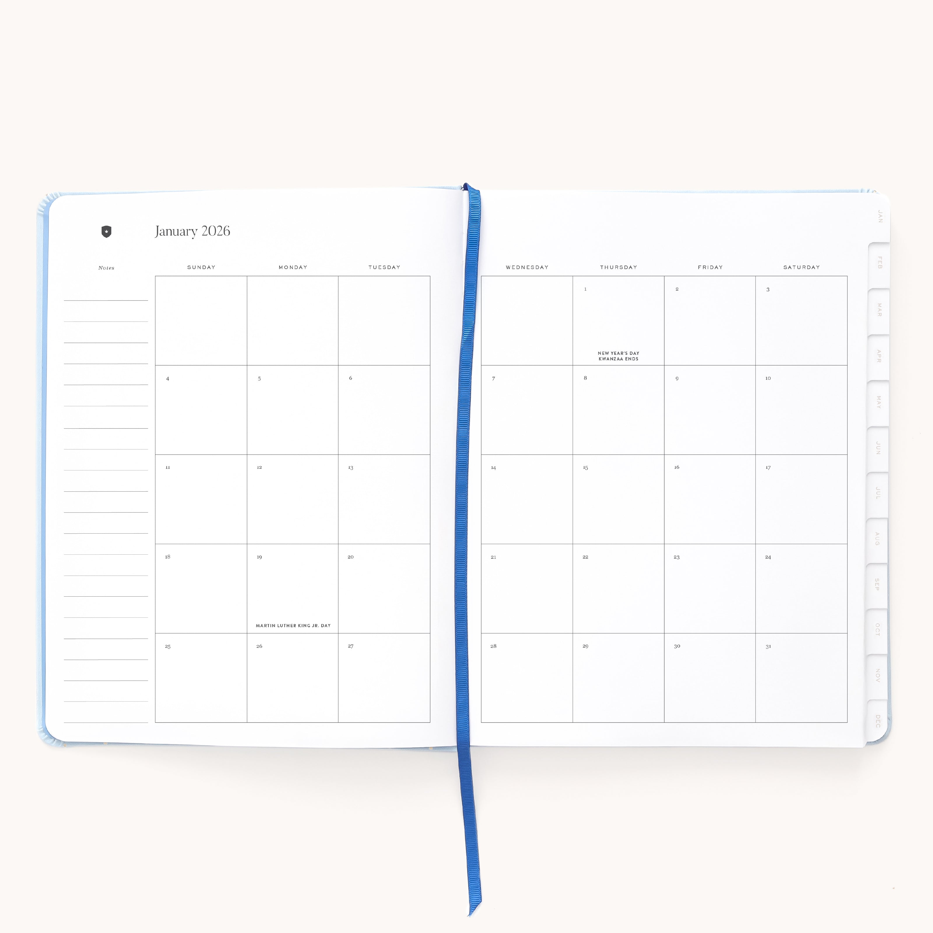 The Simplified 2026 Bookbound Weekly Dapperdesk Planner in Carolina Dot shows a monthly January calendar with a grid layout and lined notes, plus a blue ribbon bookmark for added style—perfect for elegant organization.