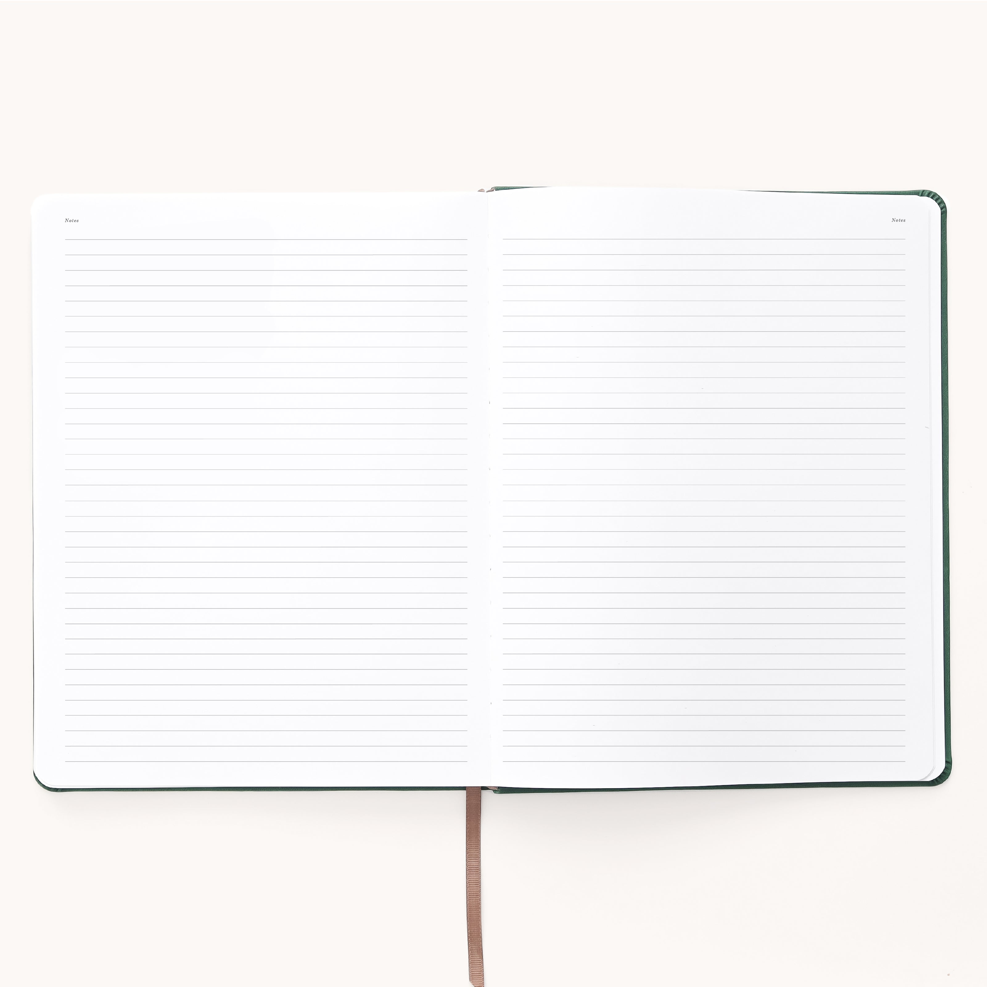 The Simplified 2026 Bookbound Weekly Dapperdesk Planner in Evergreen features a leatherette cover, brown ribbon bookmark, and open lined pages with date spaces in the corners, lying flat on a light surface.