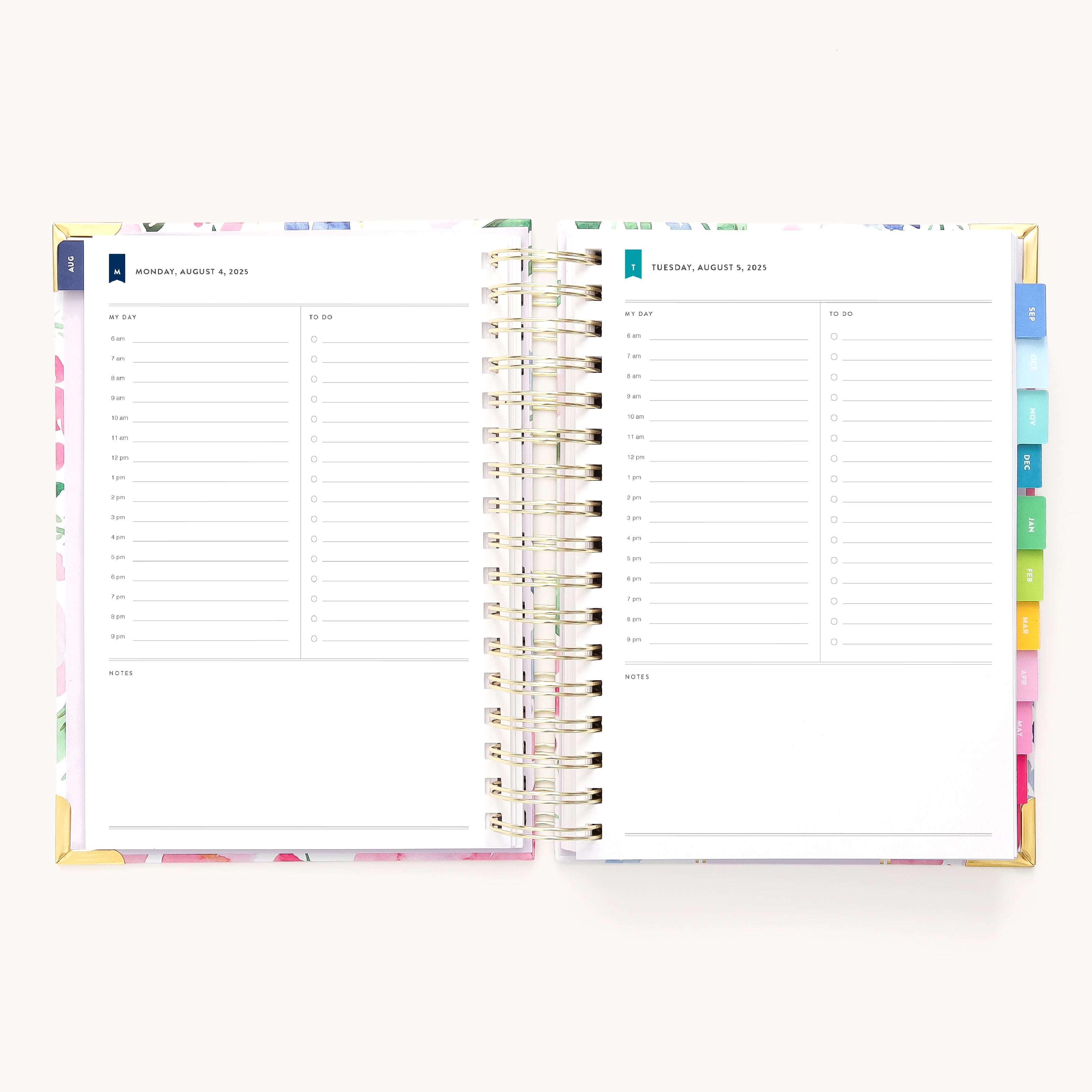 An open 2025-2026 Cottage Floral Spiral Daily Simplified Planner displays a weekly layout for August 7-8, 2023, with time slots from 6 AM to 9 PM and space for notes. Colorful tabs and gold foil details enhance its elegant gold spiral binding.