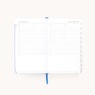The 2025-2026 Bookbound Daily Dapperdesk Planner - Carolina Dot by Simplified features an elegant leatherette finish. Open to Tuesday, August 5th and Wednesday, August 6th, the planner includes a schedule from 7 a.m. to 8 p.m., a notes section, tabbed dividers and a blue ribbon bookmark in the center.