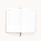 The 2025-2026 Simplified Bookbound Daily Dapperdesk Planner in Evergreen features pages with hourly slots from 7 AM to 7 PM for August 8 and 9, 2023. It includes a brown ribbon bookmark and tabs for easy navigation, offering ample space for detailed planning.