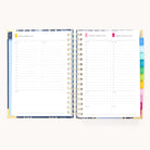 The 2025-2026 Spiral Daily Simplified Planner - Poppy Posies by Simplified features gold foil details and offers a beautifully organized schedule with hourly slots from 6 AM to 9 PM for August 12-13, 2023. It includes colorful tabs for easy navigation.
