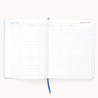 The 2025-2026 Bookbound Weekly Dapperdesk Planner - Carolina Dot by Simplified shows the week from August 4 to August 10, 2025. It includes lined note spaces under each day, tabbed sections on the right, a light blue leatherette cover, and a blue ribbon bookmark for easy navigation.