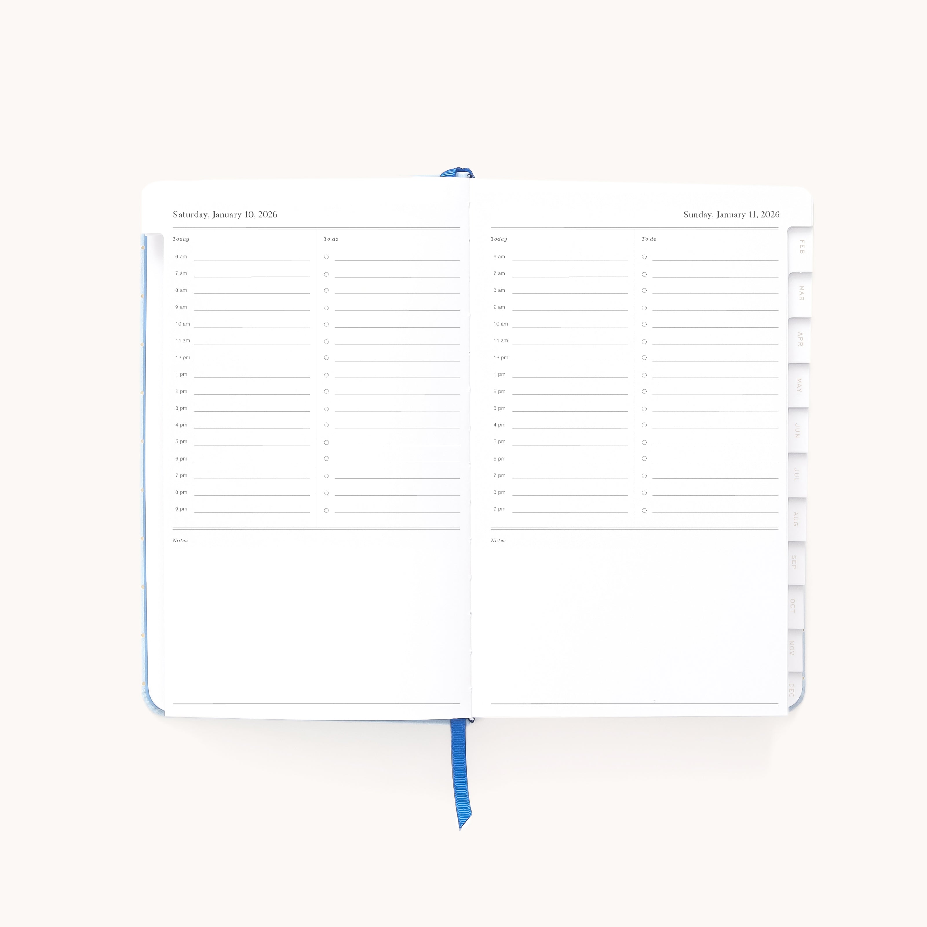 The Simplified 2026 Bookbound Daily Dapperdesk Planner in Carolina Dot has an open leatherette cover, a two-page weekly layout with hourly time slots, columns for weekend days, and a blue ribbon bookmark.