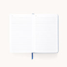 The Simplified 2025-2026 Bookbound Daily Dapperdesk Planner - Carolina Dot lies open with its lined pages against a light background, showcasing its elegant leatherette cover and featuring a blue ribbon bookmark ideal for keeping track of your daily plans.